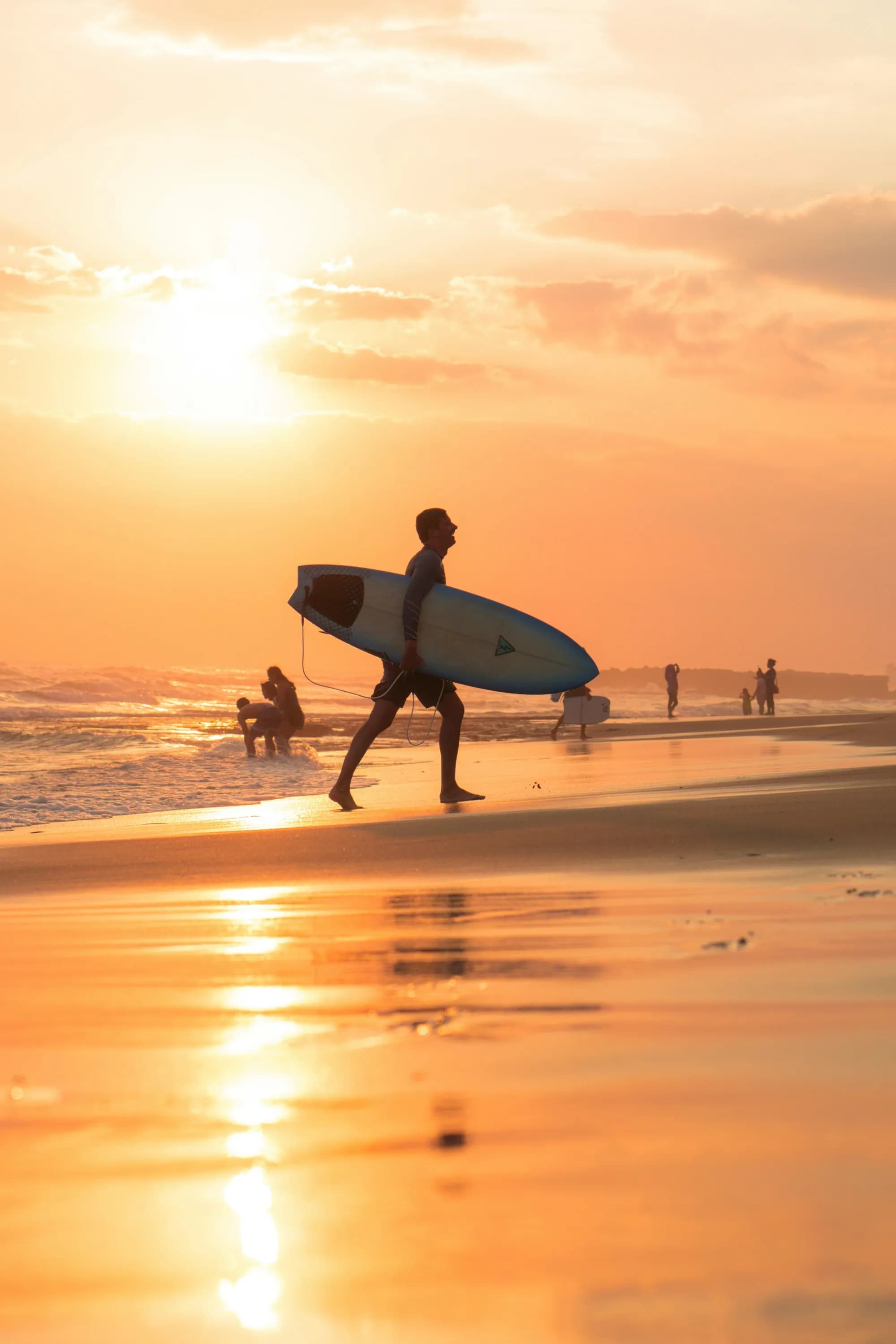 Surfer carrying a board across Canggu Beach at sunset, Bali